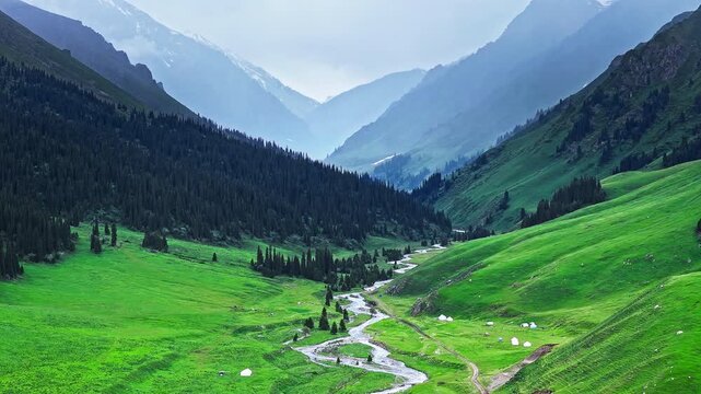 Aerial view of a winding stream flowing through a green mountain valley with a yurt camp in Xinjiang, China