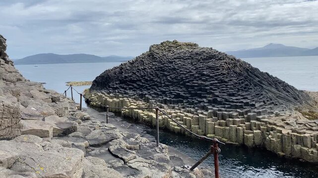 Natural basalt columns form a unique coastal landscape surrounded by grey sea and cloudy skies, Staffa, Inner Hebrides, Scotland, United Kingdom