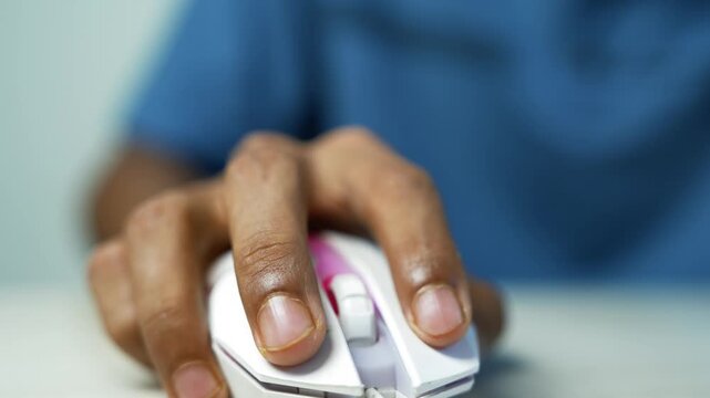 Hand Clicking White Computer Mouse, Close-up of a person's hand using a white computer mouse on a desk, with a blue shirt in the soft blurred background.