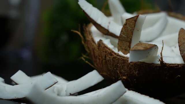 Fresh coconut pieces in a half shell with a dark blurred background, showing natural texture and tropical food detail
