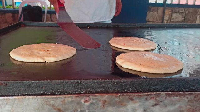 Person hands with spatula flipping artisanal pupusas on the grill. Hands preparing traditional Nicaraguan pupusas. Vendor preparing traditional grilled cheese pupusas. Nicaragua food