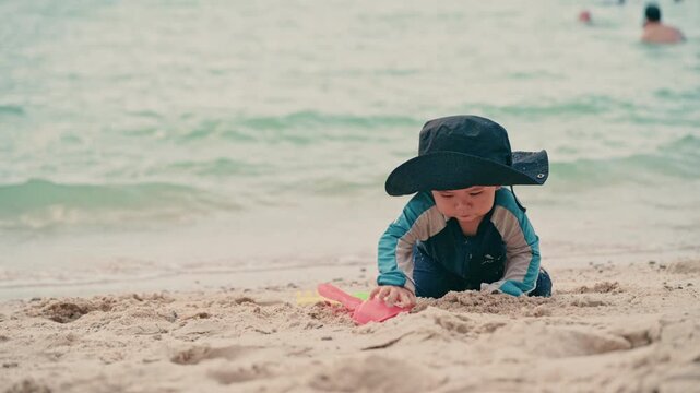 Cute baby boy with sun hat playing in the sand on a beautiful beach, close up. 
