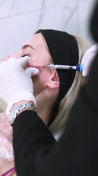 Vertical video. Dermal injection. Skin procedure. Professional female beautician hands in gloves using neurotoxin filler film in aesthetic beauty clinic.