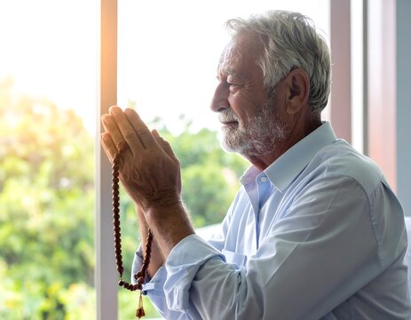 Senior Man Praying with Prayer Beads by Window