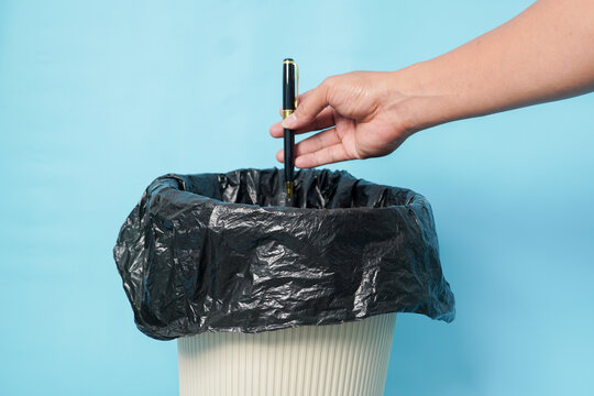 Hand dropping a black pen into a waste bin against a light blue background