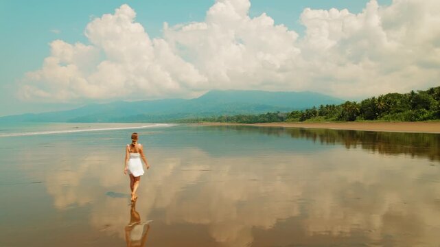 Woman walks along the reflective shore of Uvita Beach under cloudy sky in Costa Rica