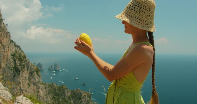 Woman admiring huge lemon above Capri island cliffs during summer coastal day