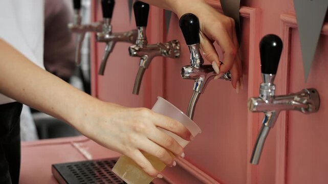 Close-up of woman opening a beverage tap and pouring a light draft drink into a plastic cup. Self-service beverage station, catering and event refreshment concept.