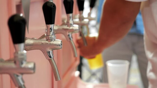 Close-up of beverage taps at a dispensing station while a worker serves drinks in the background. Draft beverage service for bar, catering, festival and event concepts.