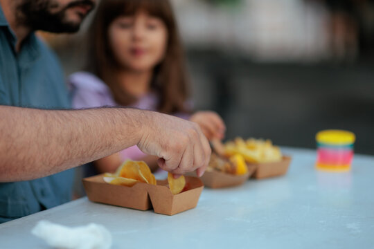 Father Hand Grabbing Snack From Paper Bowl Near Cute Little Daughter. Caring dad sharing fast food meal with his beautiful young daughter outdoors