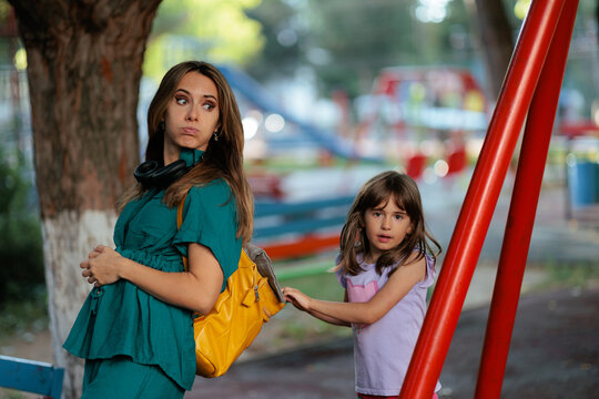Thirsty Little Girl Reaching For Water Bottle Inside Mother Yellow Backpack. Curious young daughter tries to grab water bottle from her tired mother backpack