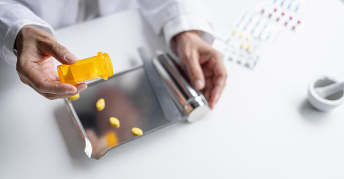 Asian senior female pharmacist counting and arranging prescription pills on stainless steel counting tray with spatula at pharmacy counter.