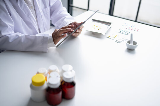 Asian senior female pharmacist using digital tablet representing modern pharmacy pharmaceutical care healthcare technology and medication safety.