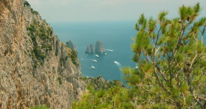 A summer view of Capri rugged coast and Faraglioni sea stacks surrounded by numerous boats