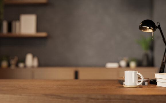 Close up of wooden desk with white mug, lamp and books in blurred modern office background.