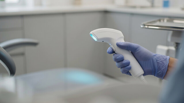dentist wearing blue glove holding handheld intraoral scanner in dental clinic
