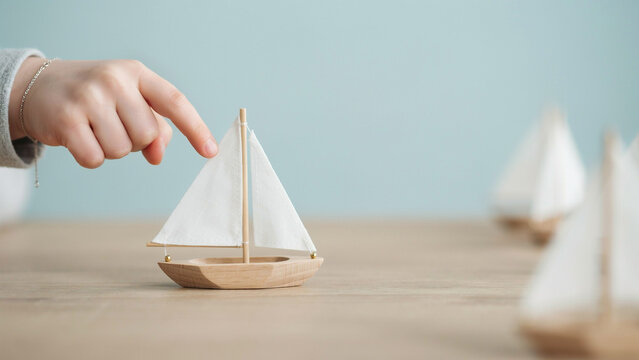 child hand touching small wooden toy sailboat on wooden table
