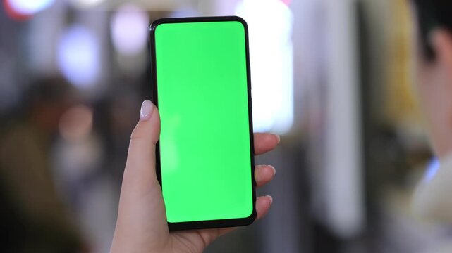 Hand holds smartphone with green screen. Background blurred with people. Three keyframes show same scene. Hand steady and centered. Urban environment visible behind