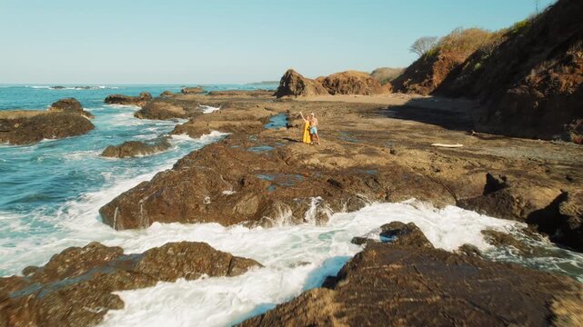 Couple standing on rocky shore with ocean waves under sunny sky in Costa Rica