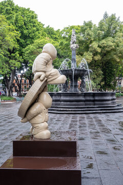 Puebla, Mexico - June 5 2026: Rodrigo de la Sierra's 'Timo' sculpture in Puebla's historic center. Fountain, trees, wet pavement.