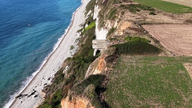 Aerial footage of a World War II concrete bunker built into the cliffs above a narrow beach on the Normandy coast, surrounded by farmland and vegetation