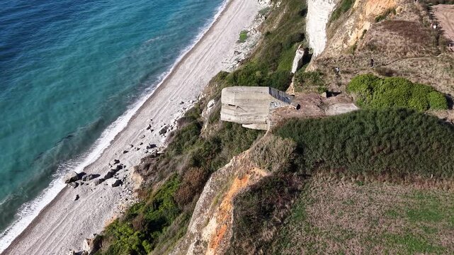World War II concrete bunker built into the cliffs above a beach on the Normandy coast, surrounded by coastal vegetation and farmland