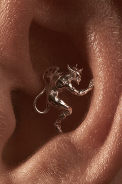 Silver devil figure earring inside human ear for unique fashion style.