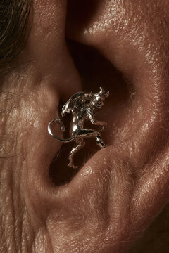 Detailed silver devil figure earring accessory clipped on human ear cartilage.