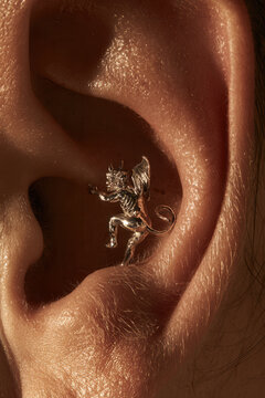 Small silver demon sculpture placed inside human ear for gothic style.