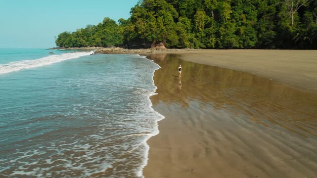 Woman in swimsuit running at tropical beach with calm ocean waves on summer day in Costa Rica
