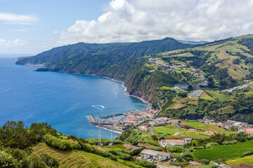 Fototapeta premium Aerial view of Povoacao, a coastal fishing village on Sao Miguel Island in the Azores, Portugal, surrounded by lush volcanic hills and the Atlantic Ocean.