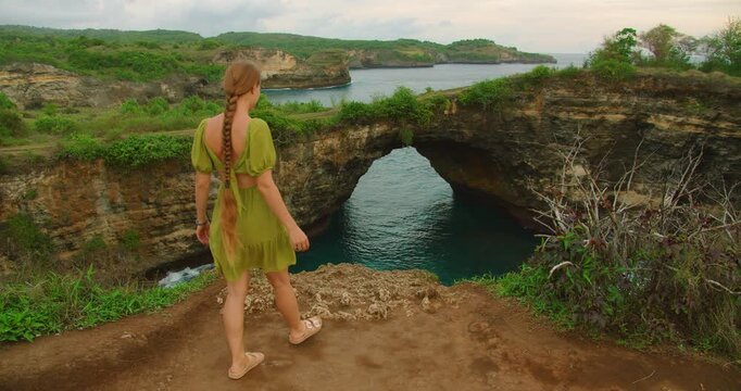 Woman walking towards stunning Broken Beach natural arch cliffside viewpoint on Nusa Penida island Bali