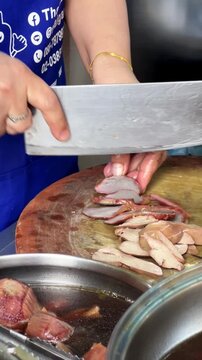 Vendor slicing tender braised duck gizzard with cleaver on wooden chopping board