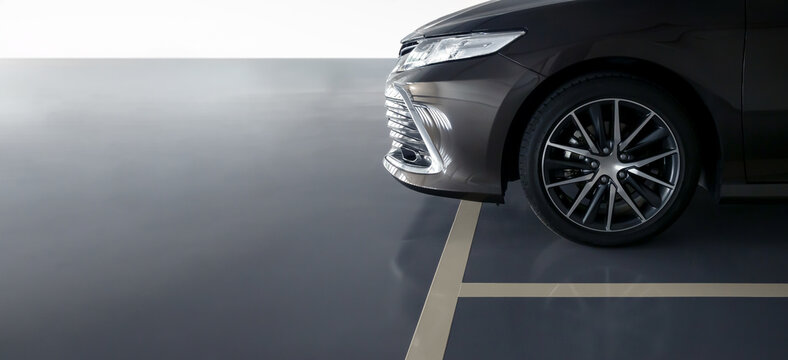 dark grey sedan front quarter view, multi-spoke alloy wheel, sleek headlight, glossy bumper, parked on reflective studio floor, cream-colored lines, parking lot, anti slip coating floor for safety