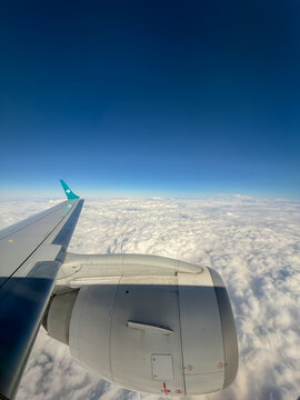Aerial view from passenger window of an Air Dolomiti airplane showing the wing, engine, and logo flying above a sea of clouds