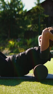 Outdoor foam rolling exercise with two people stretching on yoga mats, focusing on back relaxation, muscle recovery, and wellness in a sunny green garden setting