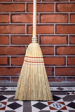 Traditional Straw Broom Against Brick Wall