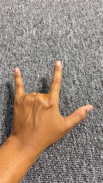 Detailed close up of a human hand making the I Love You (ILY) sign language gesture or rock symbol against a textured grey background