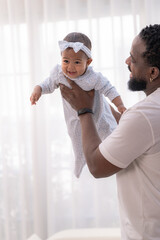 Obraz premium A devoted dad lifts his baby girl high in the air in an airy modern home, celebrating a playful bond ideal for parenting and wellbeing content full of natural candid warmth.