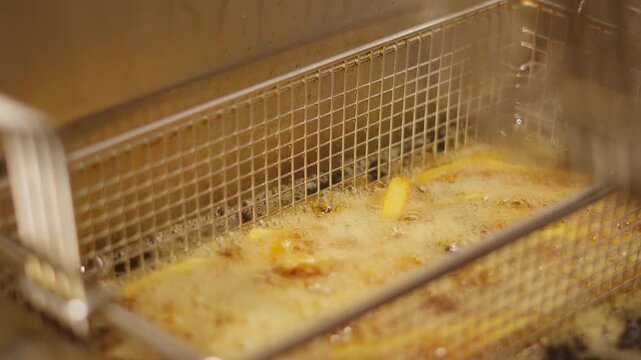 Close-up of French fries in a metal fryer basket during preparation in a commercial kitchen.