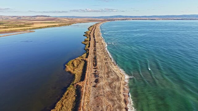 A long stretch of coastline shows land meeting the water under clear skies. Waves gently lap at the shore while grass grows along the beach.