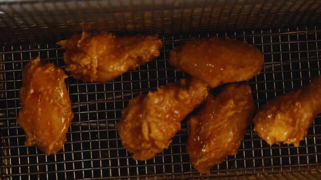 Close-up of crispy fried chicken wings with a golden coating in a metal fryer basket in a restaurant kitchen.