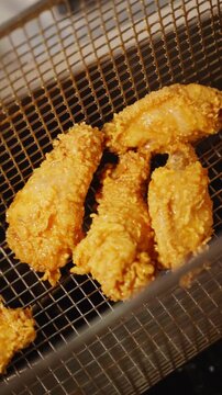 Close-up of crispy fried chicken wings with a golden coating in a metal fryer basket in a restaurant kitchen.