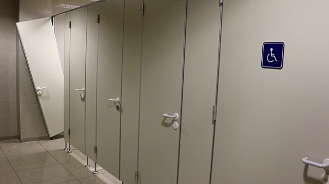 A row of doors toilet in the public restroom with the devastated door of the last cabin.