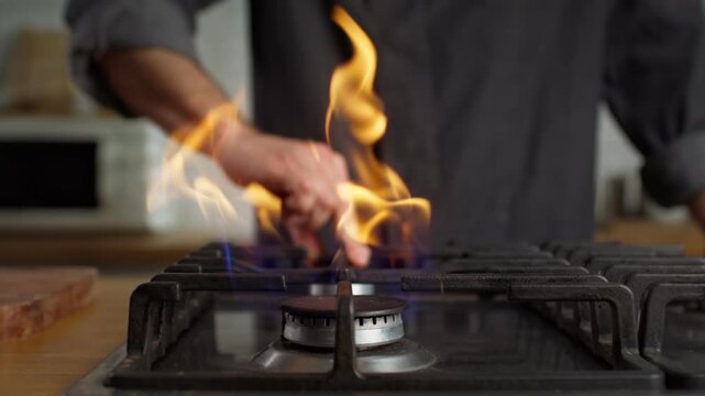 Extreme close-up of a cook turning on a gas burner as the flame ignites and rises in slow motion on a kitchen stovetop.