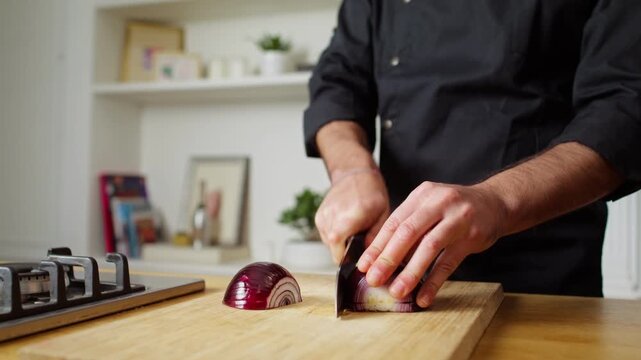 Close-up of hands slicing a red onion with a knife on a wooden cutting board in a home kitchen.