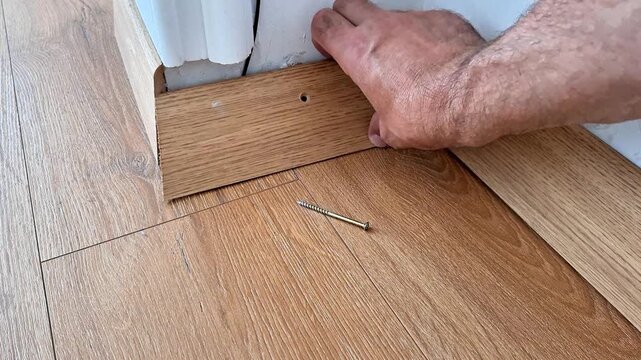 Removing old adhesive residue from a wooden baseboard during floor renovation, preparing the trim for reuse or replacement and ensuring a clean surface for installation