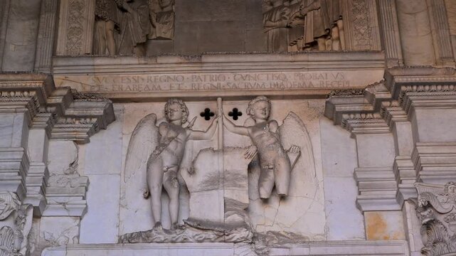 Winged putti carved in white marble hold heraldic symbols on the ornate facade of Castel Nuovo in a tight architectural detail shot.