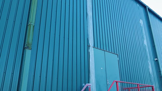 Slow tilt shows melting frozen runoff over cold metal factory doorway in winter