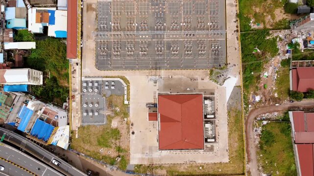 Top-down drone view of an urban electricity substation with a red-roof control building, switchgear yard, transformers and surrounding roads.